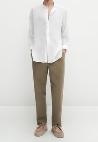Weißes Leinenhemd mit Mandarin-Kragen, kombiniert mit hellbraunen Baumwollhosen und beigen Slippern. Einfaches und entspanntes Design.