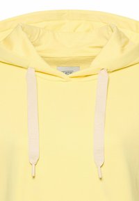 Lichtgele capuchontrui met een zachte textuur, verstelbare beige trekkoorden met gegraveerde tekst en een eenvoudig ontwerp.