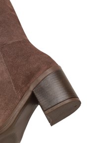 Bruine suède enkellaars met een ronde neus, een robuuste bruine hak en een gestructureerde rubberen zool. Voorzien van een glad leren afwerking aan de basis.