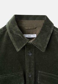 Camisa de pana de color verde oscuro con cuello puntiagudo, botones negros y dos bolsillos delanteros con solapa, de talla mediana con etiqueta de la marca visible en el interior del cuello.