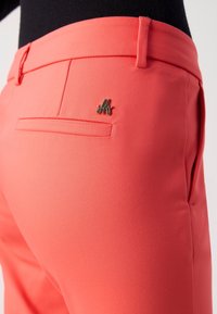 Koraalkleurige broek met hoge taille van rekbare stof, voorzien van een vlakke voorkant, een achterzak en een metalen logo-accent nabij de zak.