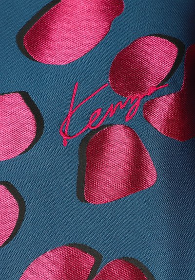 Tissu avec un fond turquoise et de grandes formes irrégulières en relief magenta et noir. "Kenz" brodé en rose vif sur le tissu.