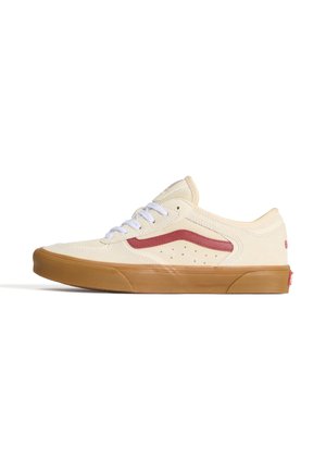 Basket basse beige avec lacets blancs, détail d'une bande rouge, côté perforé et semelle en caoutchouc marron sur fond blanc.