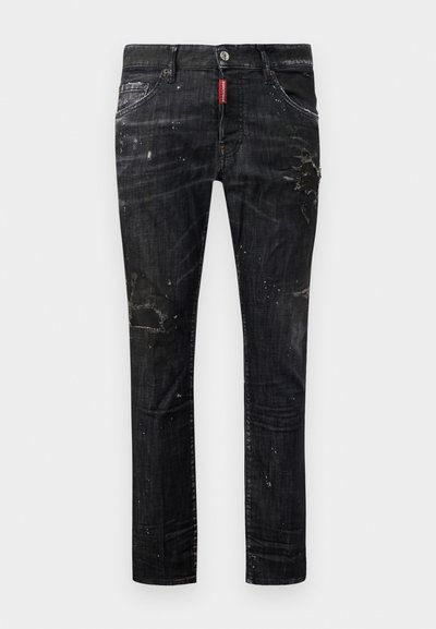 Jeans de mezclilla negra con un ajuste slim, detalles desgastados, manchas de pintura y una etiqueta roja en la cinturilla. Diseño clásico de 5 bolsillos.