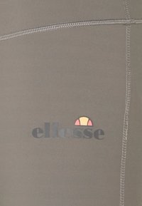 Szare elastyczne legginsy z czarnym logo "ellesse" oraz kolorową grafiką słońca. Posiadają widoczne szwy i gładką teksturę.
