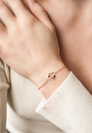 Gold-tone bracelet featuring a floral design with green and black gemstones, accented with clear crystals and a delicate chain.