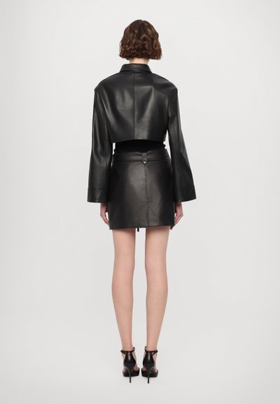 Črna usnjena kratka jakna s širokimi rokavi, v kombinaciji s krilom visoko v pasu. Gladka tekstura in minimalistična zasnova.