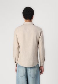 Light beige long-sleeve shirt with a collared neckline, button cuffs, and a slightly curved hem. Made of a textured linen blend fabric.