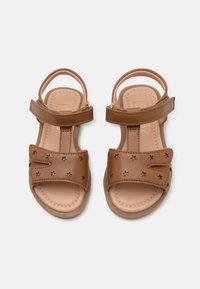 Brune skinnsandaler med stjernemønster, åpen tå, justerbare stropper og polstret såle for komfort. Flat såle, enkel design.