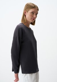 Felpa a maniche lunghe grigio scuro con scollo rotondo, fessure laterali e vestibilità rilassata, realizzata in tessuto morbido e leggero.
