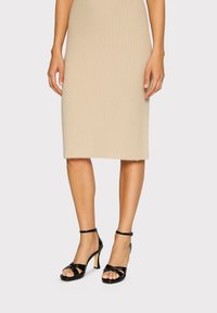 Gonna midi in maglina a coste beige con taglio dritto, abbinata a sandali con tacchi alti in pelle verniciata nera. Texture liscia e design aderente.