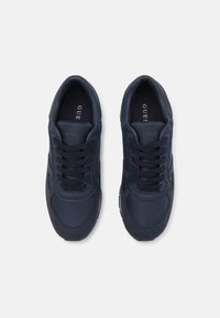 Marineblå sportsko med mesh- og ruskindteksturer, med snøring, polstret krage og en minimal logo på innersålen.