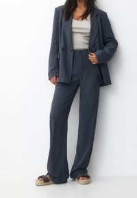 Completo blu scuro composto da un blazer doppiopetto e pantaloni a gamba larga, abbinato a una canotta grigia chiara e sandali espadrilles.