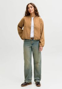 Brun bomberjakke med lynlås og struktureret finish, hvid T-shirt under, lysevidde vidde jeans med let vask, og mørkebrune slip-on sko.