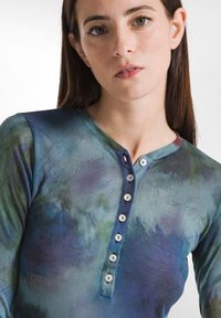 Langærmet skjorte i multicolor gradient med blå, grønne og lilla nuancer. Har henley-udskæring og seks hvide knapper. Blød tekstur.