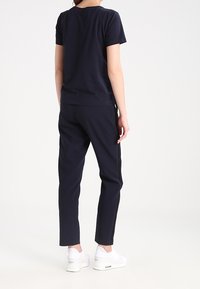 Námorně modré tričko a odpovídající kalhoty vyrobené z bavlněné směsi, s volným střihem a bílými bočními pruhy, doplněné bílými teniskami.