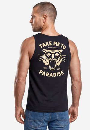 Man wearing black sleeveless shirt with beige tiger face and text "Take me to paradise" on the back, paired with blue jeans.