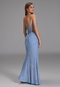 Robe longue bleue avec un corsage ajusté, tissu pailleté, fines bretelles et un panneau arrière transparent. Bas évasé avec une légère traîne.