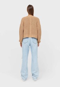 Beige gebreide trui met een verkort ontwerp, afhangende schouders en een gestructureerde achternaad. Combineer met lichtblauwe wijde jeans.