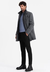 Abrigo de lana gris con cuello, superpuesto a un suéter azul claro. Pantalones negros ajustados y botas negras de tobillo. Diseño y texturas minimalistas.