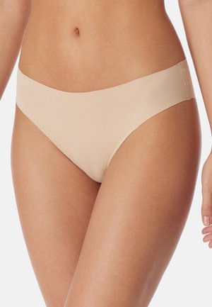 Frau trägt nahtlose, hautfarbene Bikini-Unterwäsche, gezeigt von der Taille bis zum oberen Oberschenkel vor weißem Hintergrund.