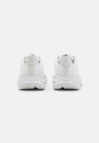 Vita atletiska skor med en strukturerad tygöverdel, dämpade sulor och en framträdande vågliknande design på yttersulan. Logotyp visas på hälen.