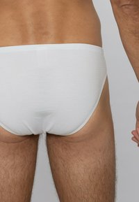 Culottes en coton blanc avec une texture côtelée. Design ajusté, taille élastique et couverture minimale. Bords lisses et silhouette classique.