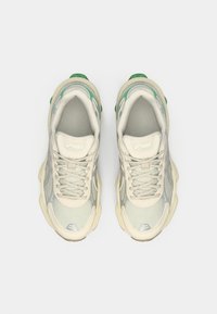 Cream-colored athletic shoes with a textured design, mesh upper, and green accents at the heel. Features a rounded toe and laces.