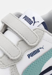 Fehér sneaker szürke suede kiegészítőkkel, türkiz csíkkal és tépőzáras pántokkal. Puma logóval a sarkán és a nyelvén. Texturált felület.