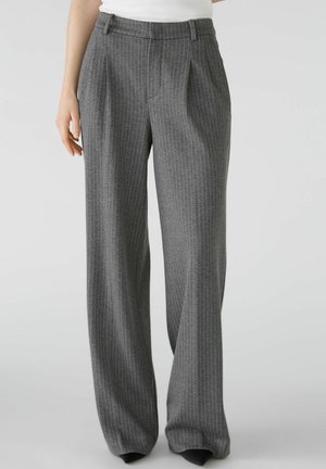 Pantalones anchos de rayas grises, combinados con una camiseta blanca metida por dentro, con pliegues y presillas para cinturón en la cintura.