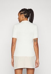 White cable-knit short-sleeve sweater featuring a fitted design. The back includes a subtle scoop neckline and ribbed texture.