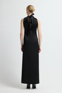 Czarna długa sukienka z satyny z kokardą zawiązaną przy szyi i odkrytymi plecami. Gładka tekstura i dopasowana sylwetka z fasonem do ziemi.