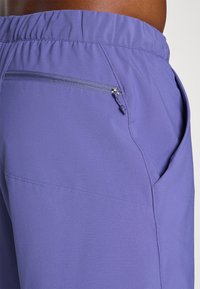 Purple athletic shorts made of lightweight material with a zippered back pocket and an elastic waistband. Smooth texture with no additional patterns.