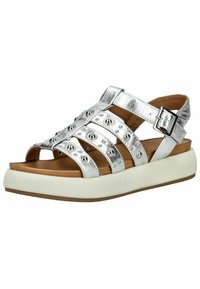 Stříbrné kovové sandály s více popruhy a dekorativními nýty, které mají polstrovanou hnědou stélku a bílou platformovou podrážku.