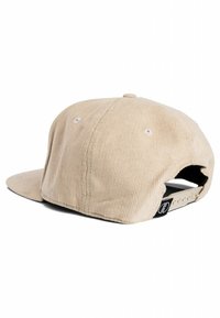 Beige corduroy cap with a flat brim and adjustable snapback. Features stitched eyelets and a black logo tag at the back.