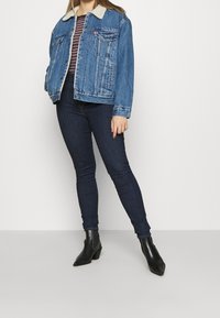 Jeansjacka med en beige pälsfoderkrage, utrustad med flera fickor framtill och en avslappnad passform. Kombinerad med mörka tajta jeans och ankelstövlar.