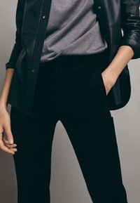 Svarta sammetbyxor har en elegant, figurnära design och sidofickor. De är kombinerade med en grå topp och en svart läderjacka.