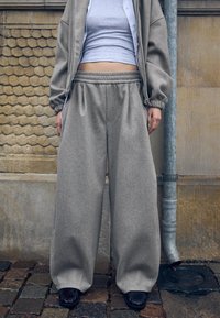 Pantaloni de trening supradimensionați gri, dintr-un material moale, cu talie elastică și buzunare laterale, asortați cu un top gri scurt.