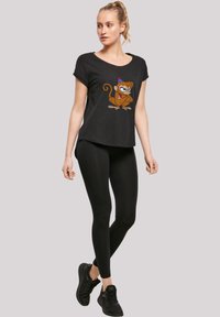 Svart T-skjorte med korte ermer og et fargerikt ape-motiv, kombinert med svarte leggings og svarte treningssko, satt mot en nøytral bakgrunn.