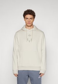 Helle beige Kapuzenpullover mit Kängurutasche, verstellbarem Kordelzug und einem dezenten Logo in der Mitte. Weicher Stoff und lockere Passform.