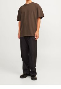 Brun oversized T-shirt med rund hals, korta ärmar, kombinerat med svarta vida byxor och svarta skor. Slät tygstruktur.