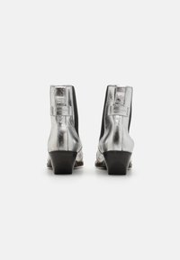 Botines metálicos plateados con un panel elástico negro, punta afilada y tacón apilado. Cuenta con un acabado texturizado en la parte trasera.