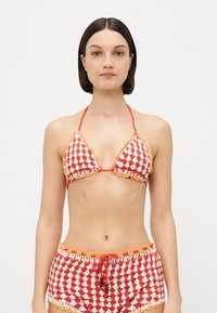 Gehaakte bikini-set met een rood en wit geruit patroon. Beschikt over driehoekige cups met golvende randen en bijpassende hoge shorts.