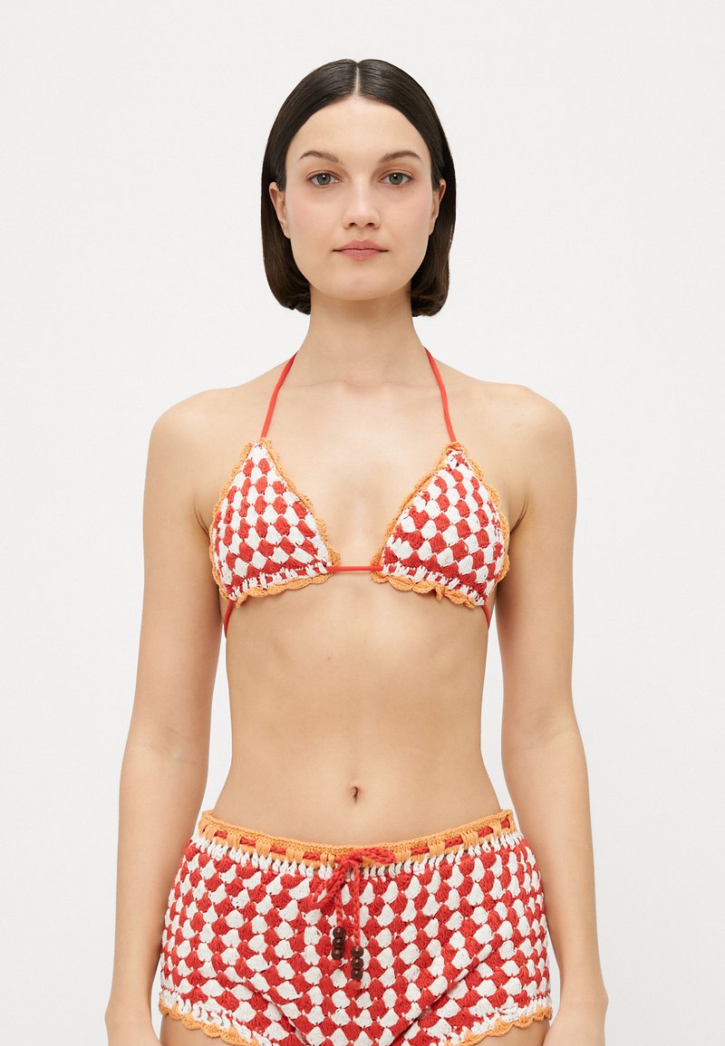 Gehaakte bikini-set met een rood en wit geruit patroon. Beschikt over driehoekige cups met golvende randen en bijpassende hoge shorts.