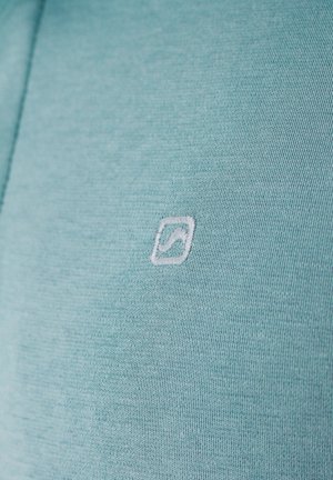 Jasnozielony materiał z małym białym haftowanym kwadratowym logo, zawierającym zakrzywioną ukośną linię w środku.