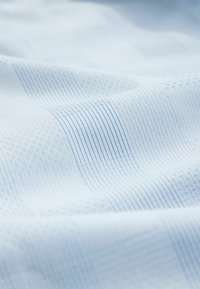 Svetlomodrá látka s rôznymi jemnými tkanými vzormi, vrátane pruhov a káro, zobrazená v jemných záhyboch.