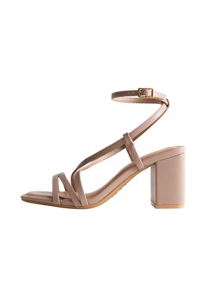 Beige high-heeled sandal with a chunky block heel, strappy design, ankle buckle, and a smooth, glossy finish on the upper material.