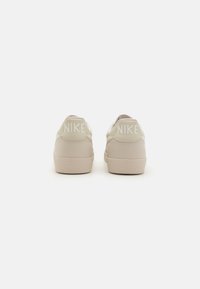 Svijetlosmeđi Nike tenisice s teksturiranim gumenenim potplatima i utisnutim logotipom na peti. Glatki materijal s čistim, minimalnim dizajnom.