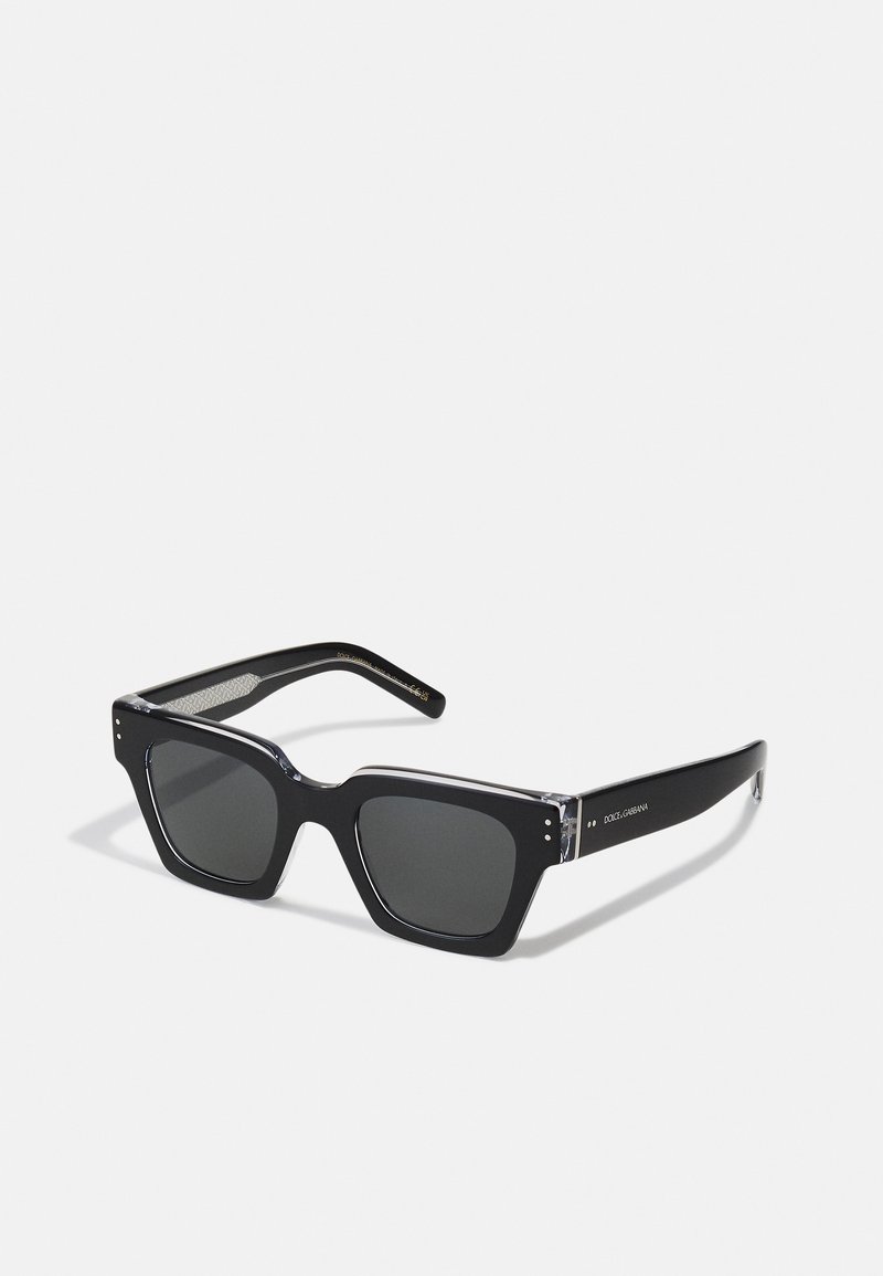 Black square-frame sunglasses with gray lenses. Clear accents on the brow and temples, featuring small decorative studs. Textured inner temple.