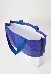 Blå og hvit totebag, laget av slitesterk vevd plast, med to blå håndtak og åpen topp, med en glatt indre tekstur.